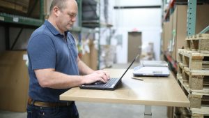 Logistics manager planning shipments on a laptop in a warehouse