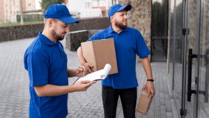 Two uniformed couriers check a delivery note and parcels outside a building before setting off. It reflects how same day delivery Manchester services rely on careful handling, accurate booking details and proof of delivery.
